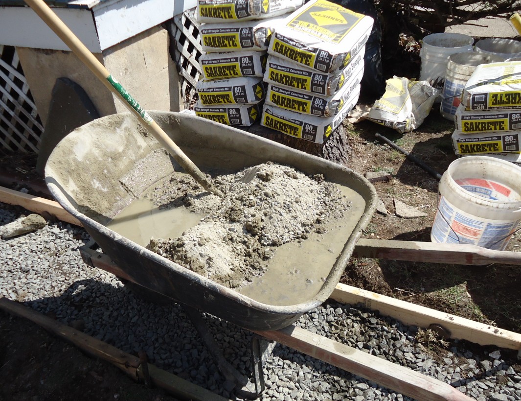 Concrete mixed in a wheelbarrow next to a stack of Sakrete bags, beside the forms for a sidewalk