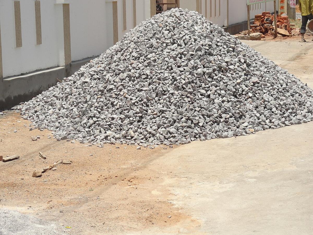 A large pile of grey crushed stone dumped beside a building site