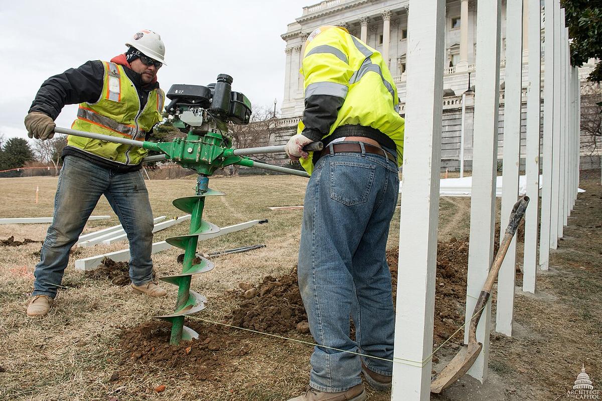 Two workers digging a fence post hole with a gas-powered auger