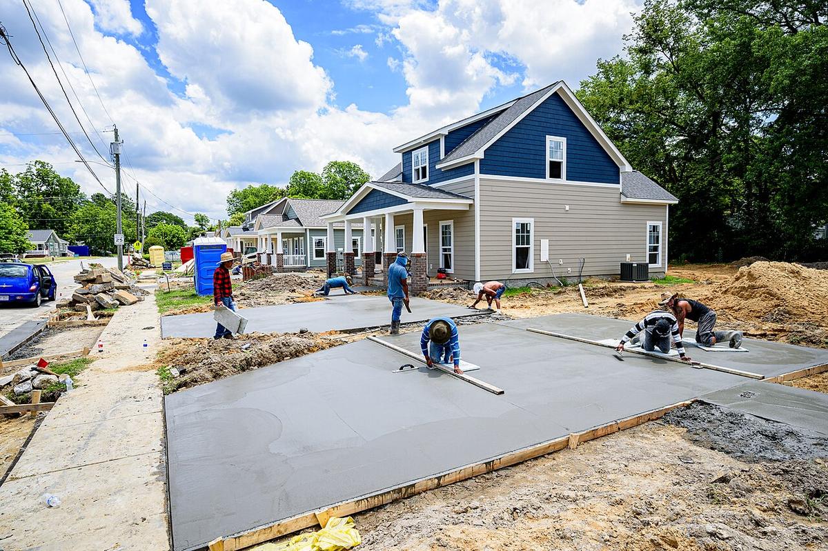 Workers finishing freshly poured concrete slabs in front of new houses