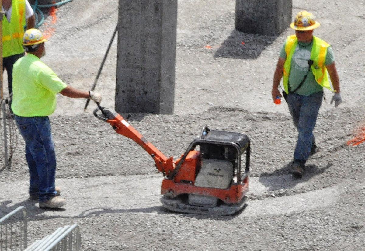 A worker guiding a plate compactor across a gravel base on a construction site